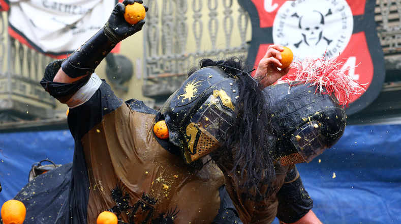 En Italia, miembros de un equipo rival son golpeados por las naranjas durante una batalla anaranjada anual del carnaval en la ciudad italiana norteña de Ivrea.